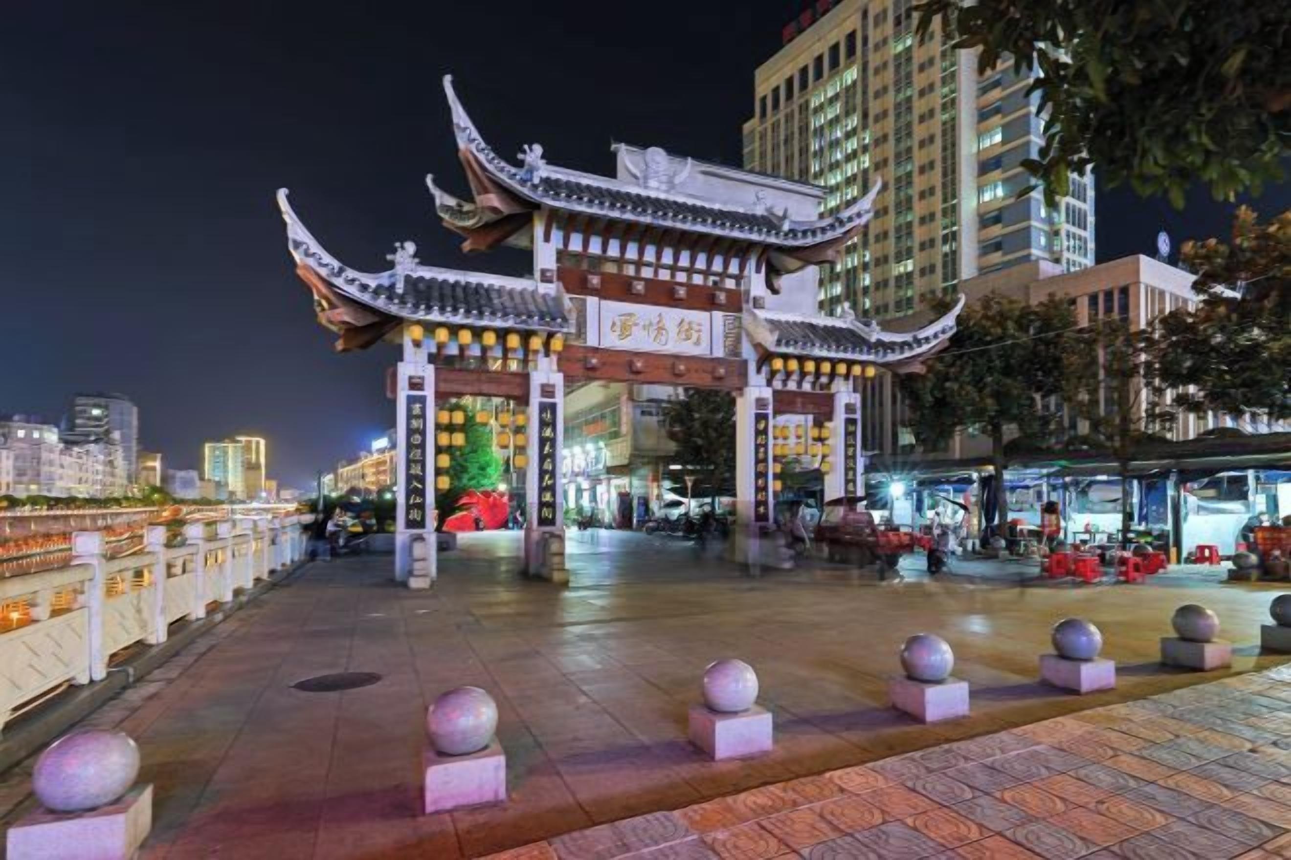 Una puerta tradicional china con arquitectura ornamentada, un camino empedrado y un edificio moderno al fondo.