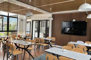 Un comedor moderno con mesas y sillas, un televisor de pantalla plana en la pared, y amplias ventanas con vistas al exterior.