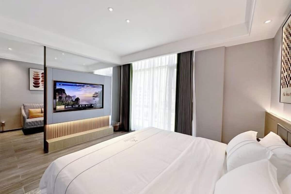 Une chambre d’hôtel moderne dotée d’un grand lit, d’un téléviseur à écran plat fixé au mur, d’un canapé et d’une grande fenêtre avec des rideaux.
