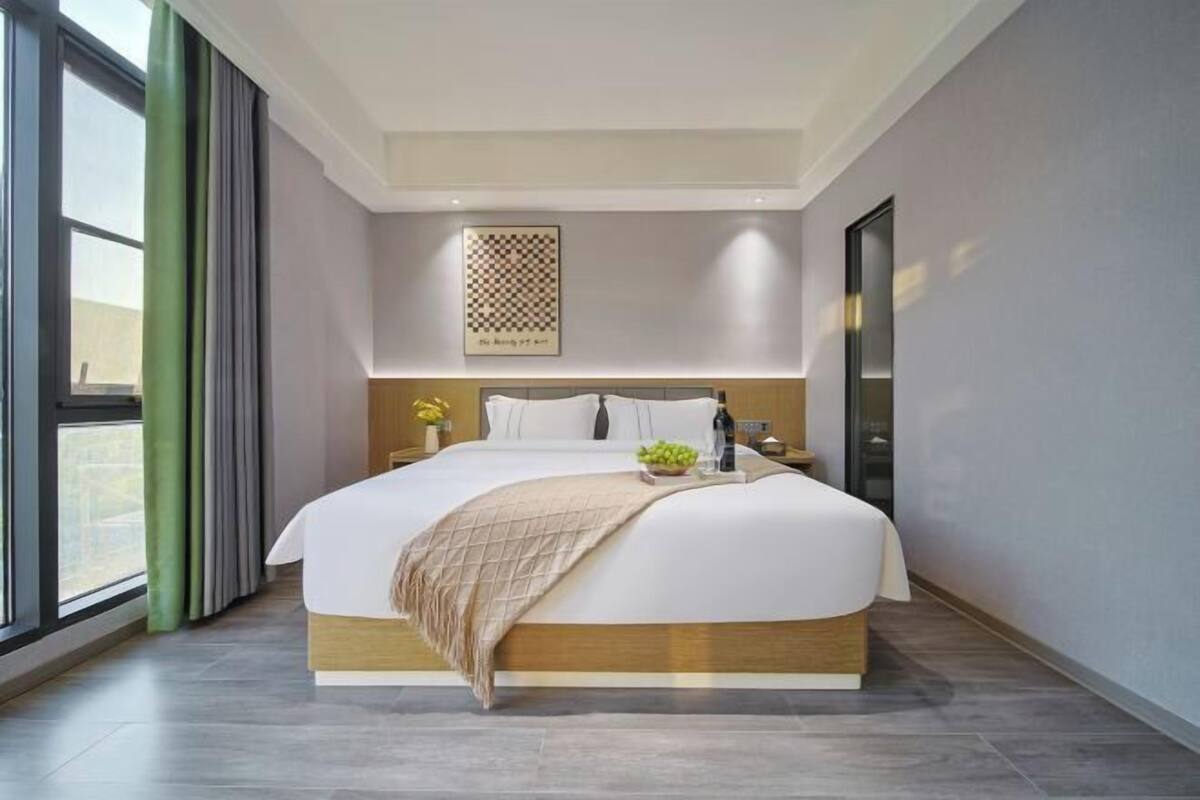 Une chambre d’hôtel moderne avec un grand lit, une vue par la fenêtre et une œuvre d’art encadrée au mur.