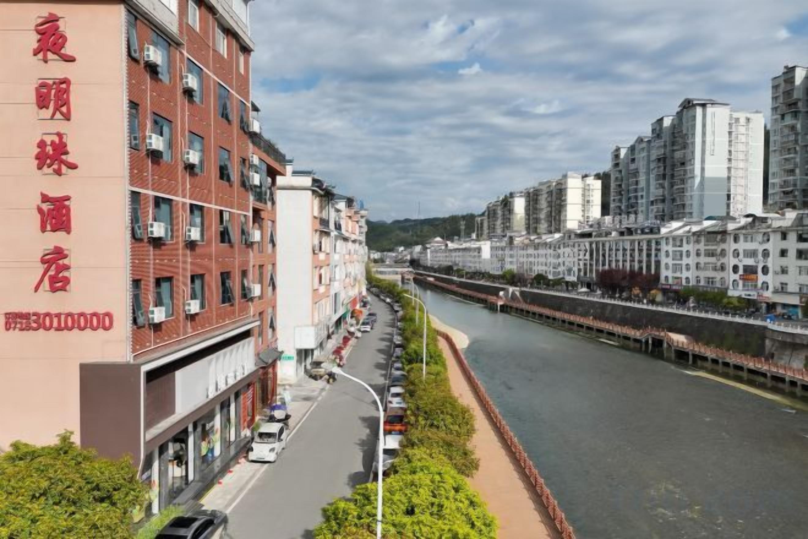 A multi-story building with a prominent red sign on the left, a river running alongside, and a bridge in the background.