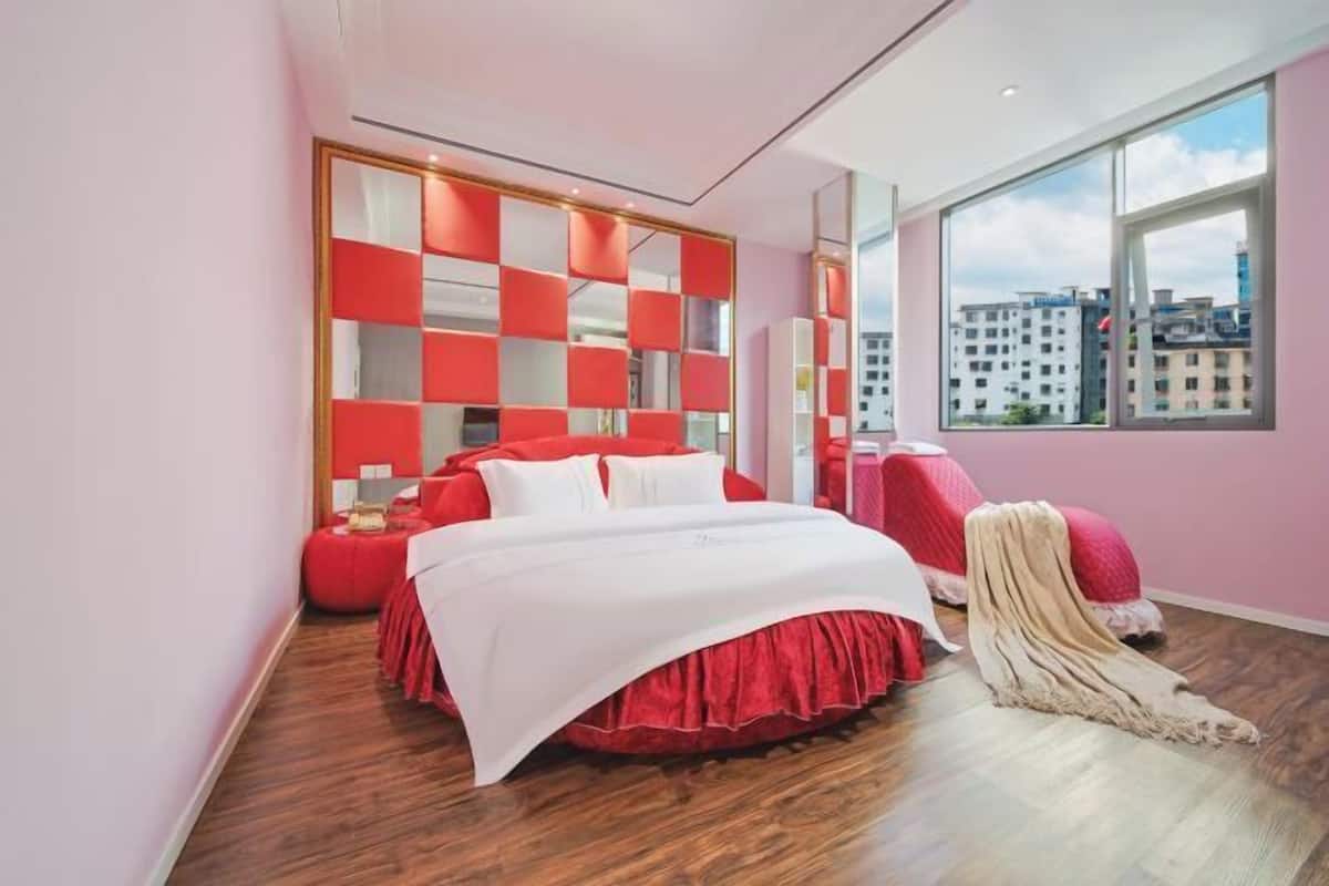 Une chambre moderne avec un grand lit, un mur d’accent rouge et une vue sur la ville.