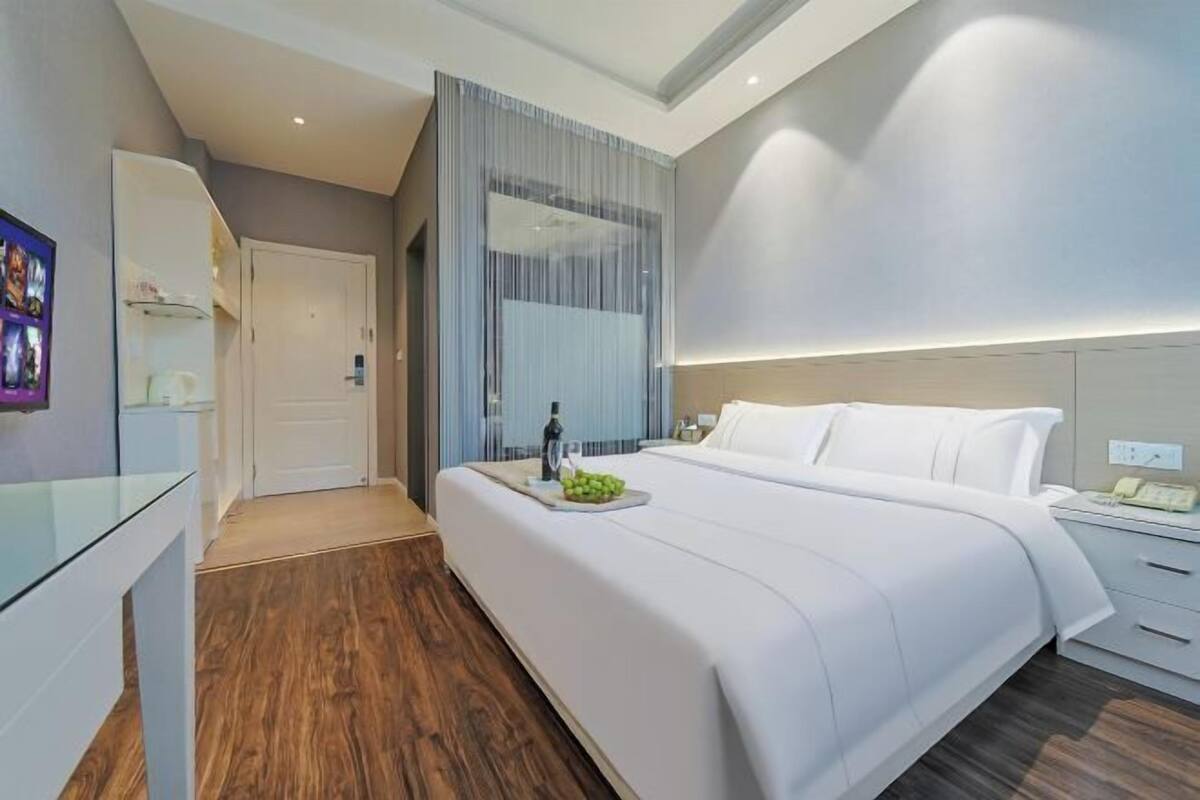 Une chambre d’hôtel moderne avec un grand lit, une table de chevet, un miroir et un plancher en bois.