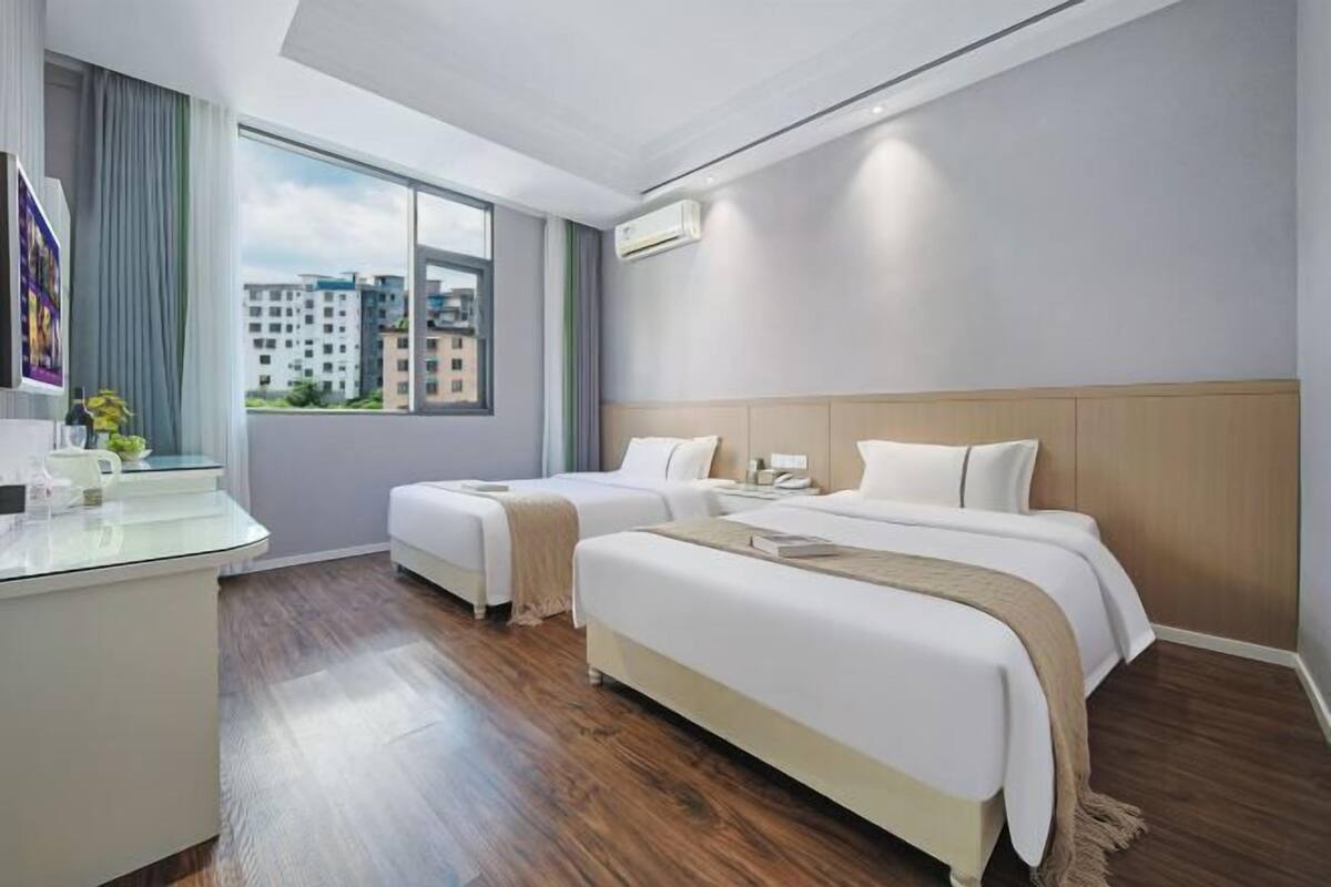 Une chambre d’hôtel avec deux lits, un bureau et une grande fenêtre donnant sur la ville.