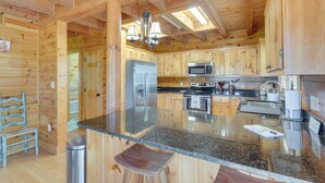 Une cuisine rustique aménagée dans une cabane en bois, avec un plan de travail en granit, des appareils en acier inoxydable et un luminaire suspendu.