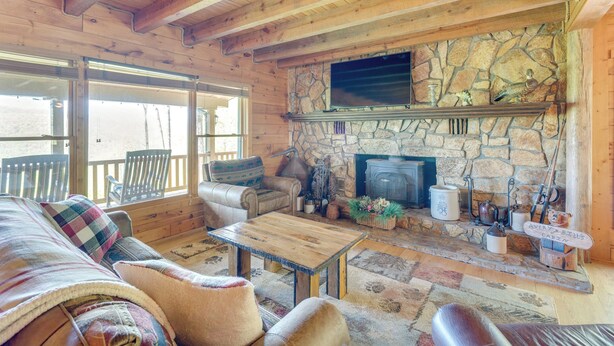 L’intérieur chaleureux d’un chalet avec une cheminée en pierre, des meubles en bois et un téléviseur fixé au-dessus.