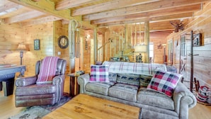L’intérieur chaleureux d’un chalet avec un fauteuil en cuir, un canapé agrémenté de coussins à motifs, une table basse en bois et un plafond en bois rustique.