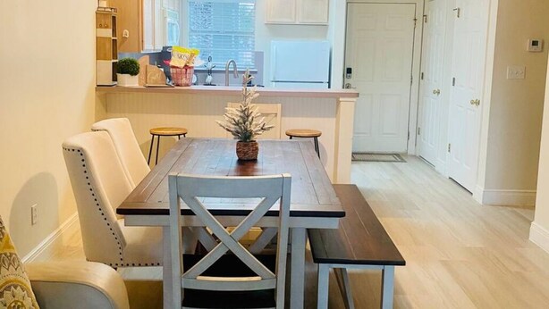 Una cocina moderna con armarios blancos, una mesa de comedor de madera y piso de madera clara.