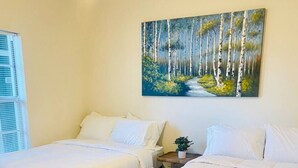 Un dormitorio con dos camas, un cuadro de un bosque y una ventana con persianas.