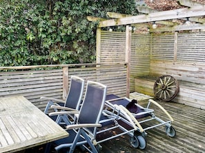 A wooden deck with a table and chairs, a wheelbarrow, and a wooden fence with climbing plants.