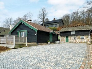 A traditional wooden building with a stone wall extension, a paved courtyard, and a metal gate.