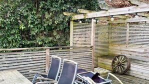 A wooden deck with a table and chairs, a wheelbarrow, and a wooden fence with climbing plants. - 4 Star Holiday Home in Bastad (Bastad)