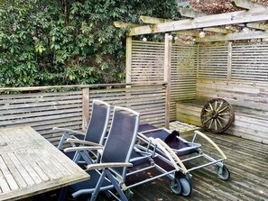 Eine Holzterrasse mit Tisch und Stühlen, einem Schubkarren und einem Holzzaun mit Kletterpflanzen.