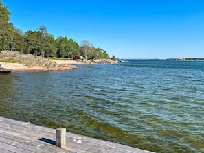 Une jetée en bois s’étendant sur un lac paisible, bordé d’une rive rocheuse et d’arbres.