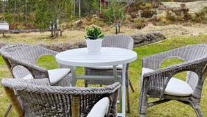 A round outdoor table with wicker chairs, surrounded by a forested area. - 4 Person Holiday Home in Graso (Gräsö)