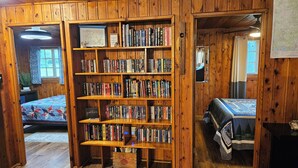 Un chalet confortable avec une bibliothèque en bois remplie de livres, un lit recouvert d’une courtepointe et un intérieur rustique en bois.