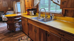 Une cuisine rustique aménagée dans une cabane en bois, avec un évier, un grille-pain et une fenêtre donnant sur la verdure.