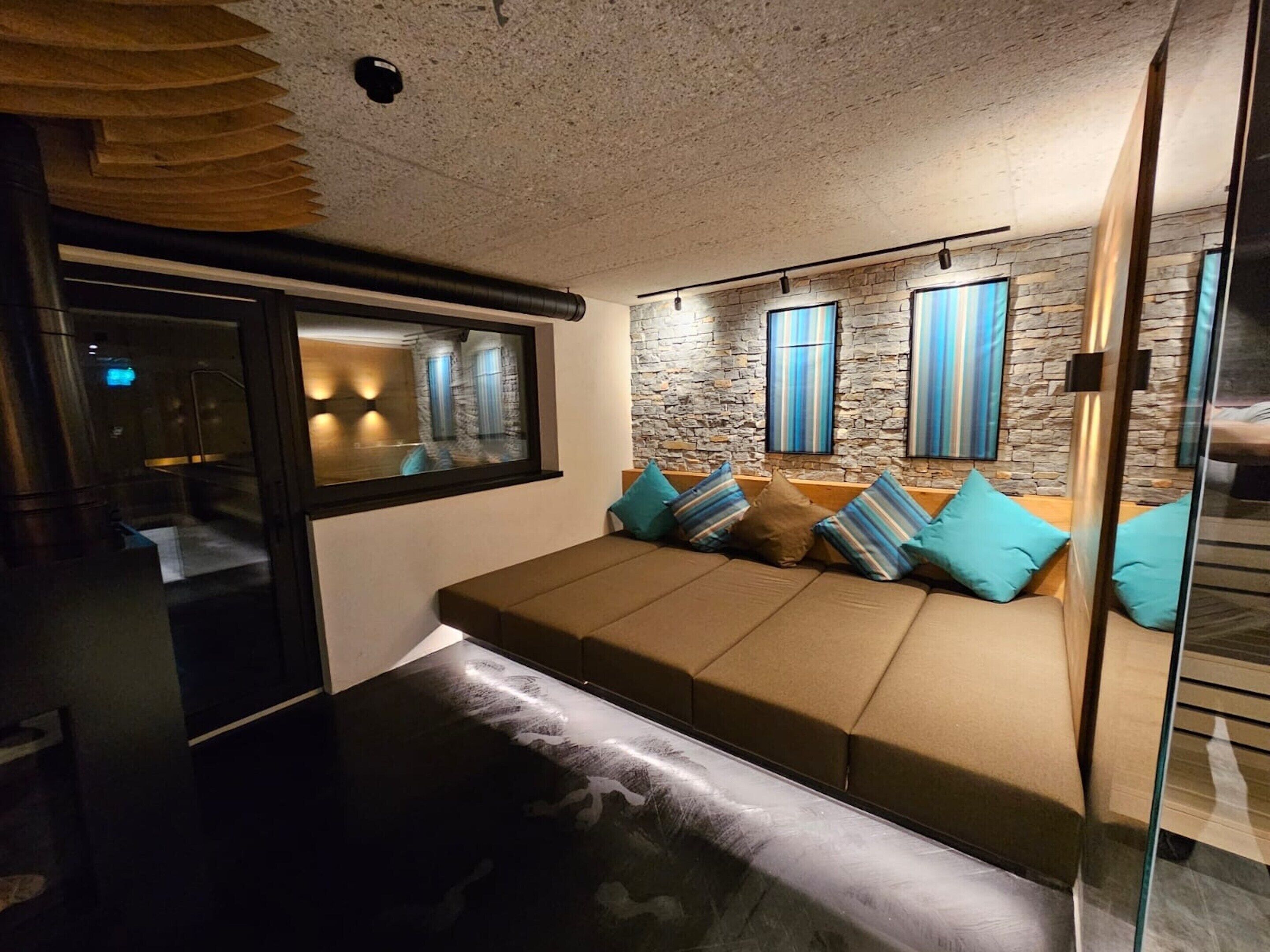 Ein modernes Wohnzimmer mit einer Sofagarnitur, einer Glastrennwand und einer Steinwand mit Fenstern.