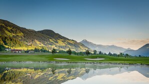 A serene lakeside view with a golf course, a church, and a mountain backdrop. - Chalet in Zillertal Near Ski Slopes & Whirlpool (Aschau Im Zillertal)