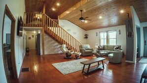 A spacious living room with a wooden staircase, a ceiling fan, and a large window providing natural light. - Spring Discounted Rates!  
Spacious w/hot tub/grill/firepit 4 BR Red River Gorge (Rogers)