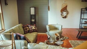 A living room with a sofa, armchair, and coffee table. There is a mirror on the wall and a shelf with decorative items. - Spring Discounted Rates!  
Spacious w/hot tub/grill/firepit 4 BR Red River Gorge (Rogers)