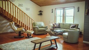 A spacious living room with a wooden staircase, a green sofa, a white armchair, and a coffee table. - Spring Discounted Rates!  
Spacious w/hot tub/grill/firepit 4 BR Red River Gorge (Rogers)