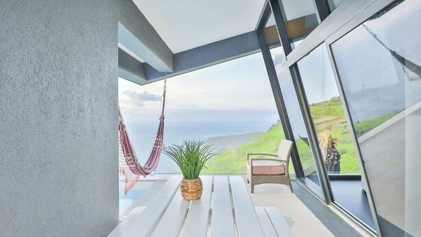 Un balcon avec un hamac, une plante en pot et une chaise d’où l’on peut admirer le paysage.