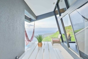Un balcon avec un hamac, une plante en pot et une chaise d’où l’on peut admirer le paysage.