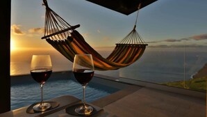 Un hamac et deux verres à vin sur un balcon donnant sur un coucher de soleil.