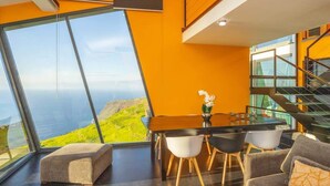 Un intérieur moderne avec une grande baie vitrée panoramique, un coin repas comprenant une table et des chaises, et un escalier.