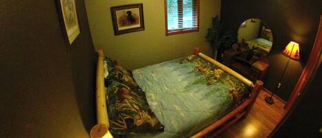A bedroom with a bed, a bedside lamp, a window with blinds, a mirror, and a framed picture on the wall.