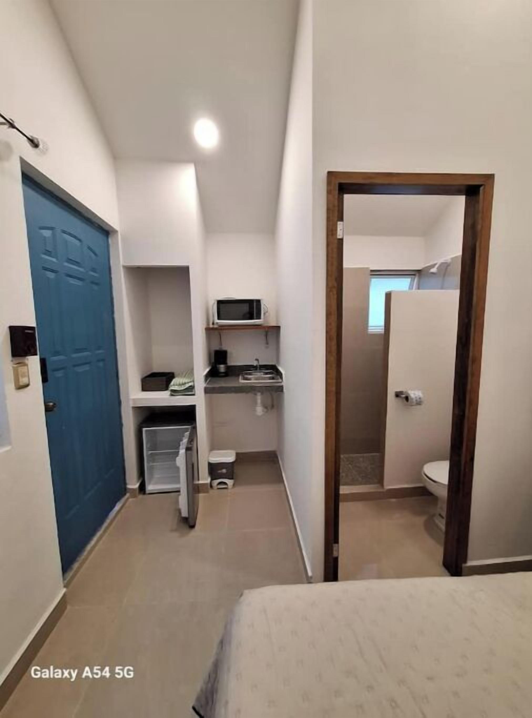 A compact hotel room with a kitchenette, a blue door, and a visible bathroom.