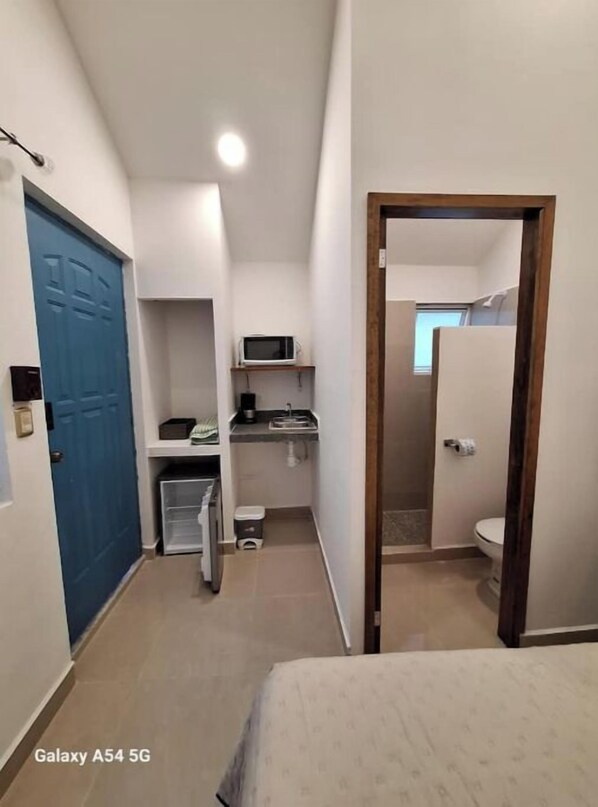 A compact hotel room with a kitchenette, a blue door, and a visible bathroom.