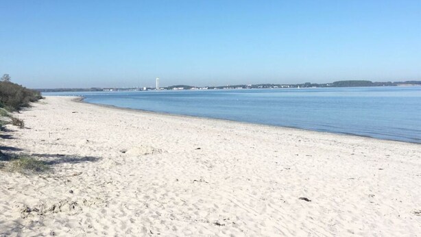 Une plage de sable fin, sous un ciel bleu clair et avec une eau calme.