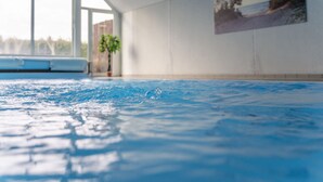 Une piscine intérieure à l’eau claire, dotée de grandes fenêtres et ornée d’un tableau accroché au mur.