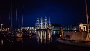 Un port de plaisance de nuit, avec plusieurs bateaux amarrés, dont un imposant voilier.
