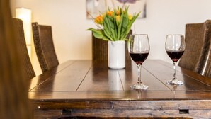 Une table de salle à manger en bois, avec deux verres à vin et un vase de fleurs.