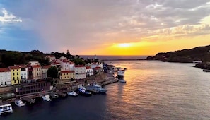A coastal town with buildings along the waterfront, boats docked, and a sunset in the background. - VERY NICE 2 ROOMS NEAR THE SEA (Port-Vendres)