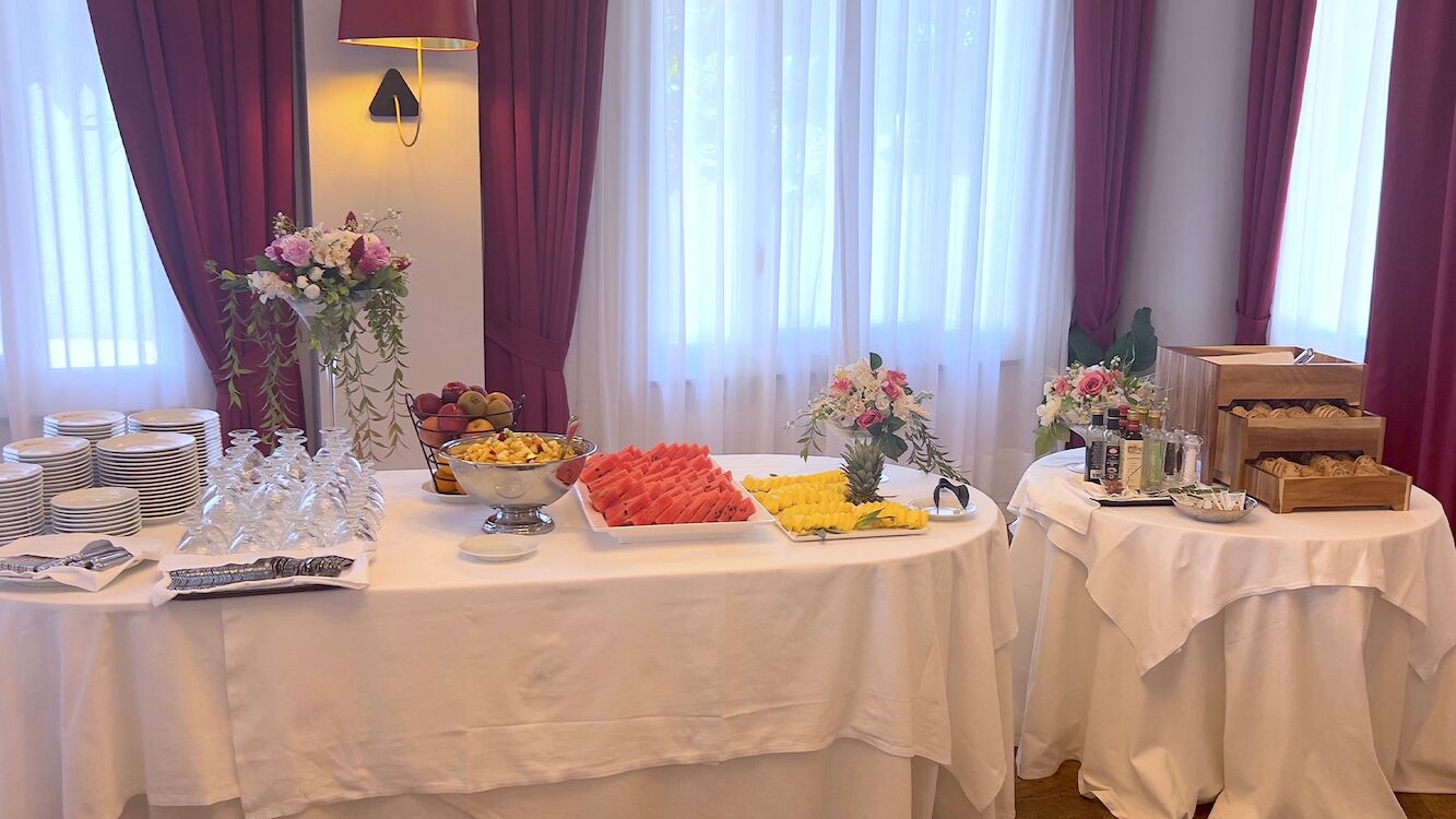 A buffet table with various food items and beverages, surrounded by curtains and floral arrangements.