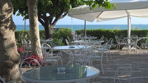 Un área de estar al aire libre con mesas redondas y sillas blancas, con vista al mar.