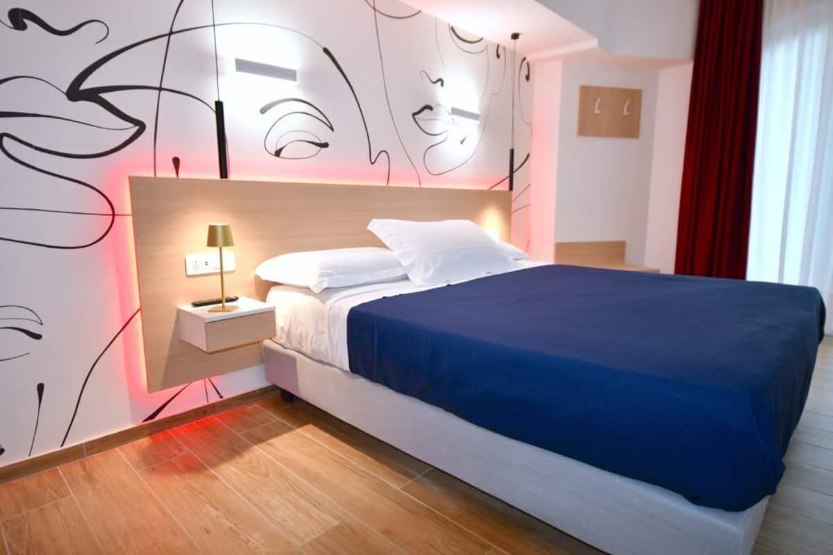 Et moderne hotelværelse med en stor seng, et natbord med en lampe, og abstrakt vægkunst.