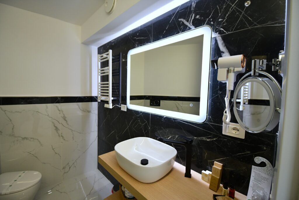 Une salle de bain avec un lavabo blanc, des murs en marbre noir, un miroir et un porte-serviettes.