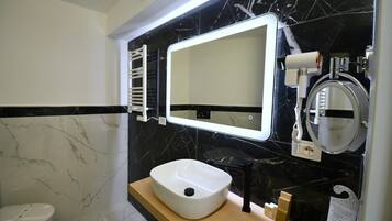 Une salle de bain avec un lavabo blanc, des murs en marbre noir, un miroir et un porte-serviettes.