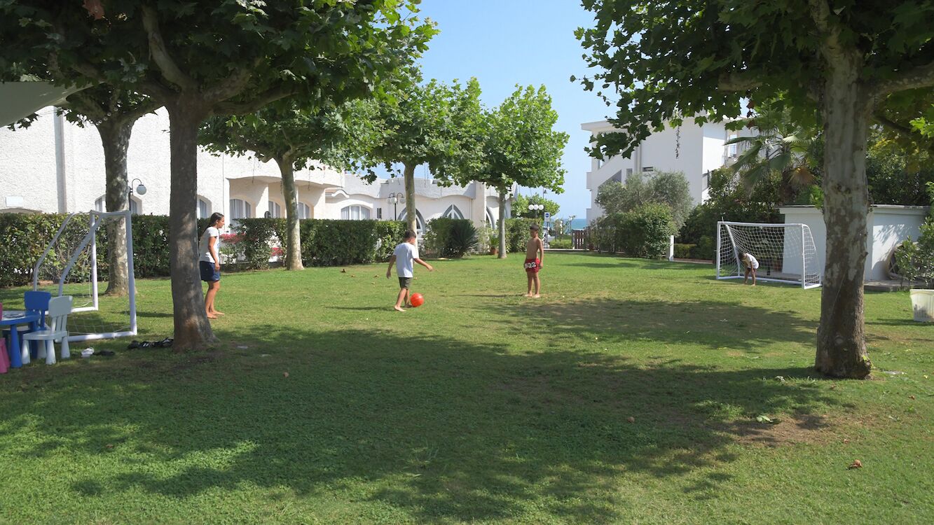 Un espacio al aire libre con césped, árboles, un arco de fútbol y un edificio al fondo.