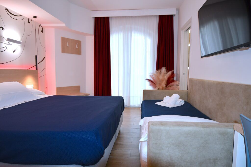 A hotel room with two beds, a TV, a desk, and a window with curtains.