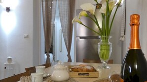 Une table à manger ornée d’un vase de fleurs blanches, d’une bouteille de champagne et d’une théière.