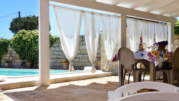 Un espace extérieur aménagé avec des sièges, protégé du soleil, et une piscine en arrière-plan.