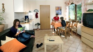 A living room with a sofa, a dining table with chairs, a kitchen area, and a television. - Inviting Apartment in Partschins/rabland (Enkirch)