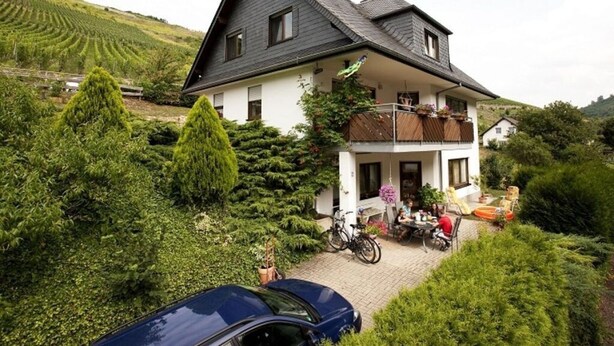 A two-story house with a balcony, surrounded by lush greenery and a vineyard in the background. - Inviting Apartment in Partschins/rabland (Enkirch)