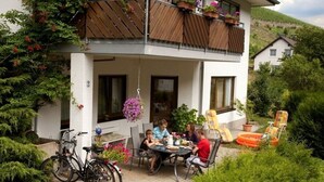 A two-story house with a balcony, outdoor seating area, and a bicycle parked outside. - Inviting Apartment in Partschins/rabland (Enkirch)
